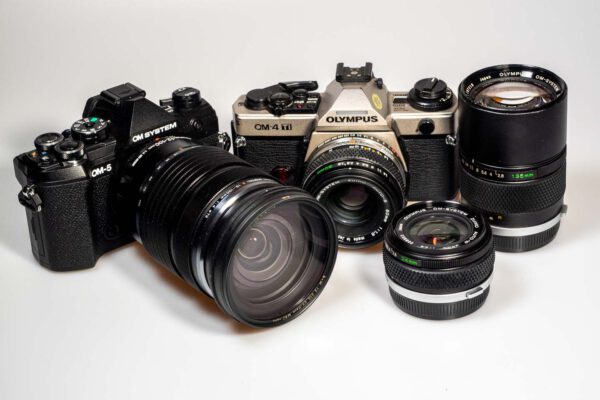 Produktfoto zeigt OM System OM-5 DSLM und Olympus OM-4 Ti, jeweils mit Objektiven